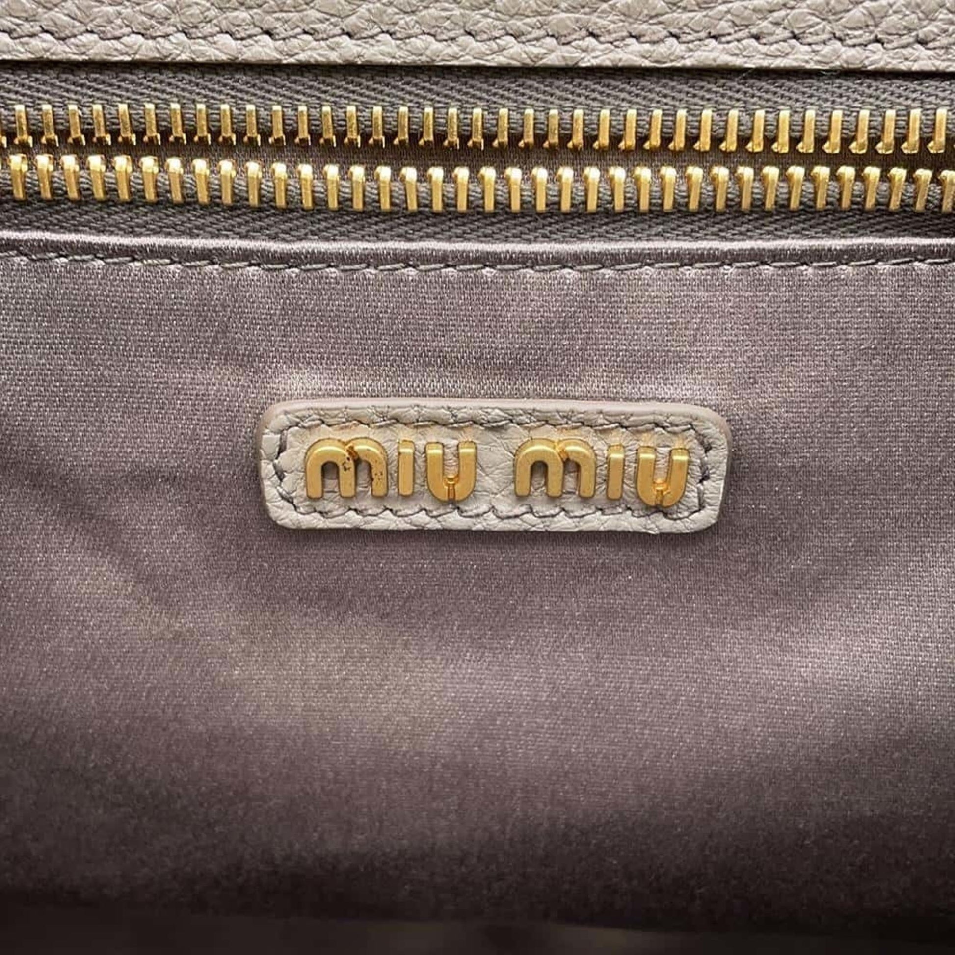 Close-up of a Miu Miu pre-owned bag featuring a gold zipper and logo detail