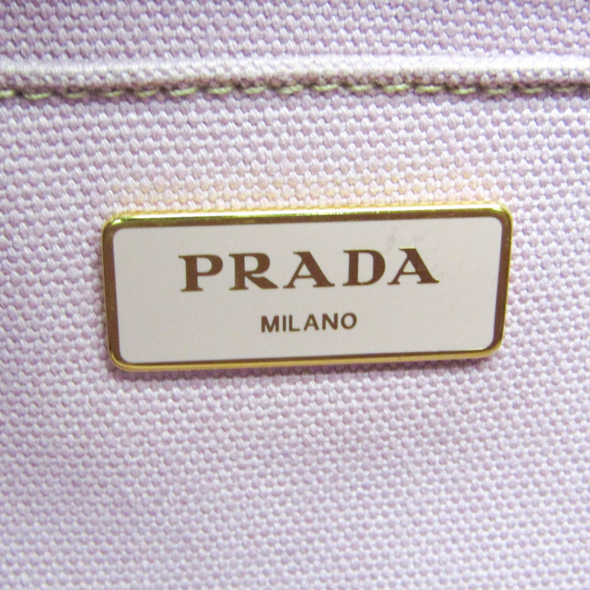 Close-up of PRADA Pre-Loved Canapa bag showing the signature PRADA MILANO label in gold detailing